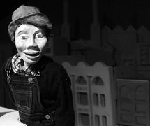 Sidekick Joe, en <em>One Way Street</em> (2010), por Small World Theatre (Cardigan, Gales, Reino Unido), un thriller clásico de cine negro con títeres para adultos, concepción y fabricación: Bill Hamblett, Outside Eye (ojo externo): Liz Walker, actores: Bill Hamblett, Ann Shrosbree, Debbie Woolley, Toby Downing. Altura del títere de Sam Stone: 2,0 m. Teatro de sombras, títeres de varillas, títeres de manipulación directa, multimédia (animación, proyección, archivo de imágenes de película y sonido). Se creó una aplicación (“app”) para el espectáculo para que el público pudiera convertirse en un personaje de la obra. Foto: Sam Vicary